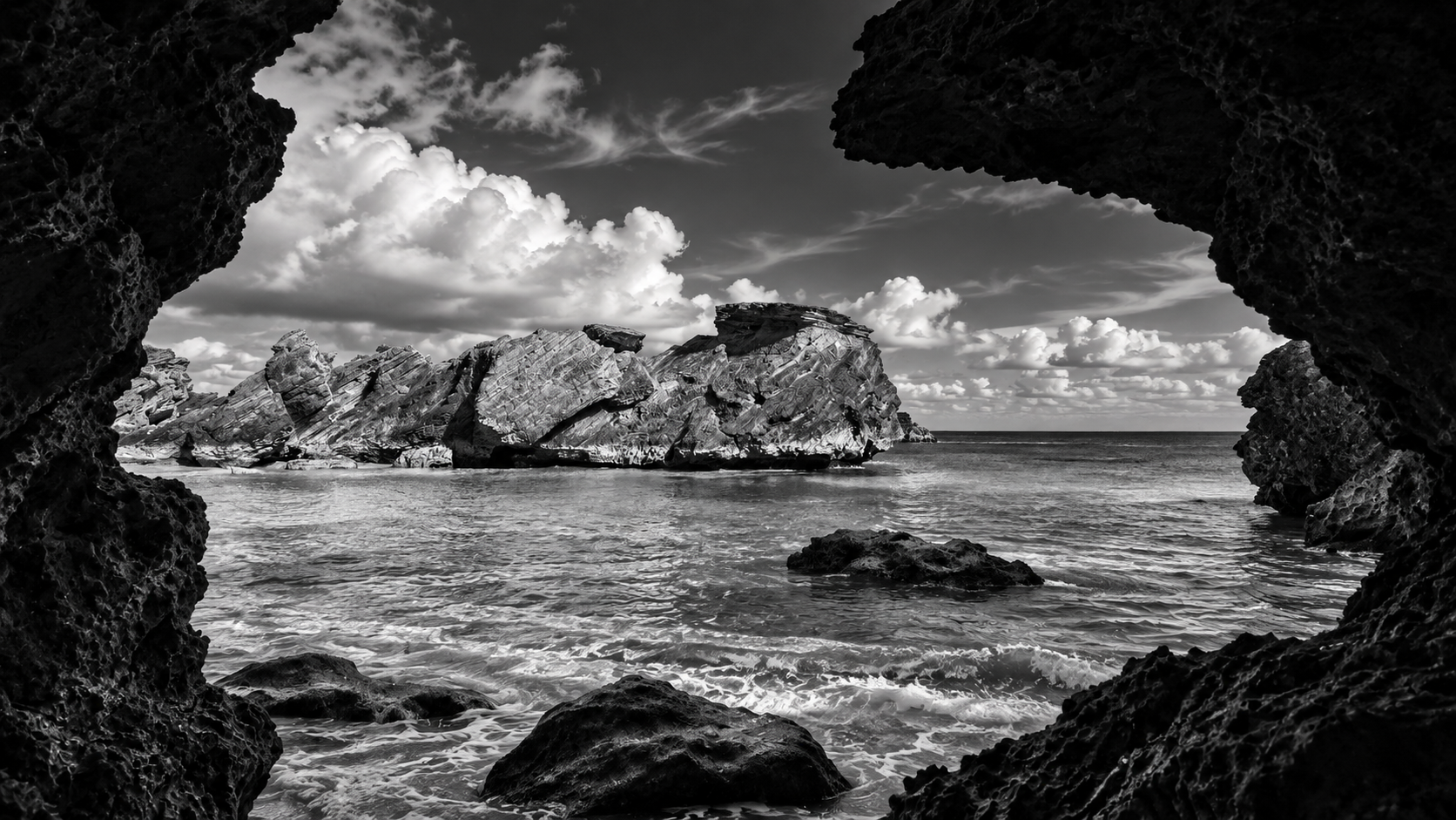Black-and-white view of a rocky Bermuda beach through a natural cave opening